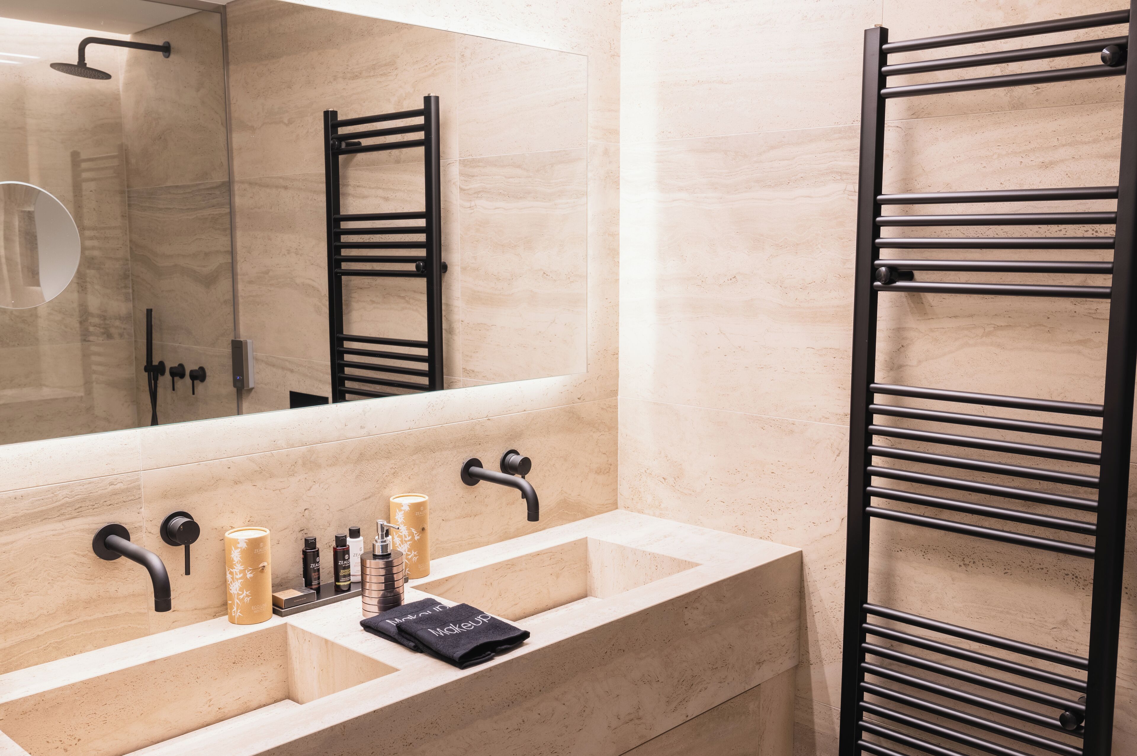 A modern bathroom with a large mirror, two sinks, and a black towel rack.