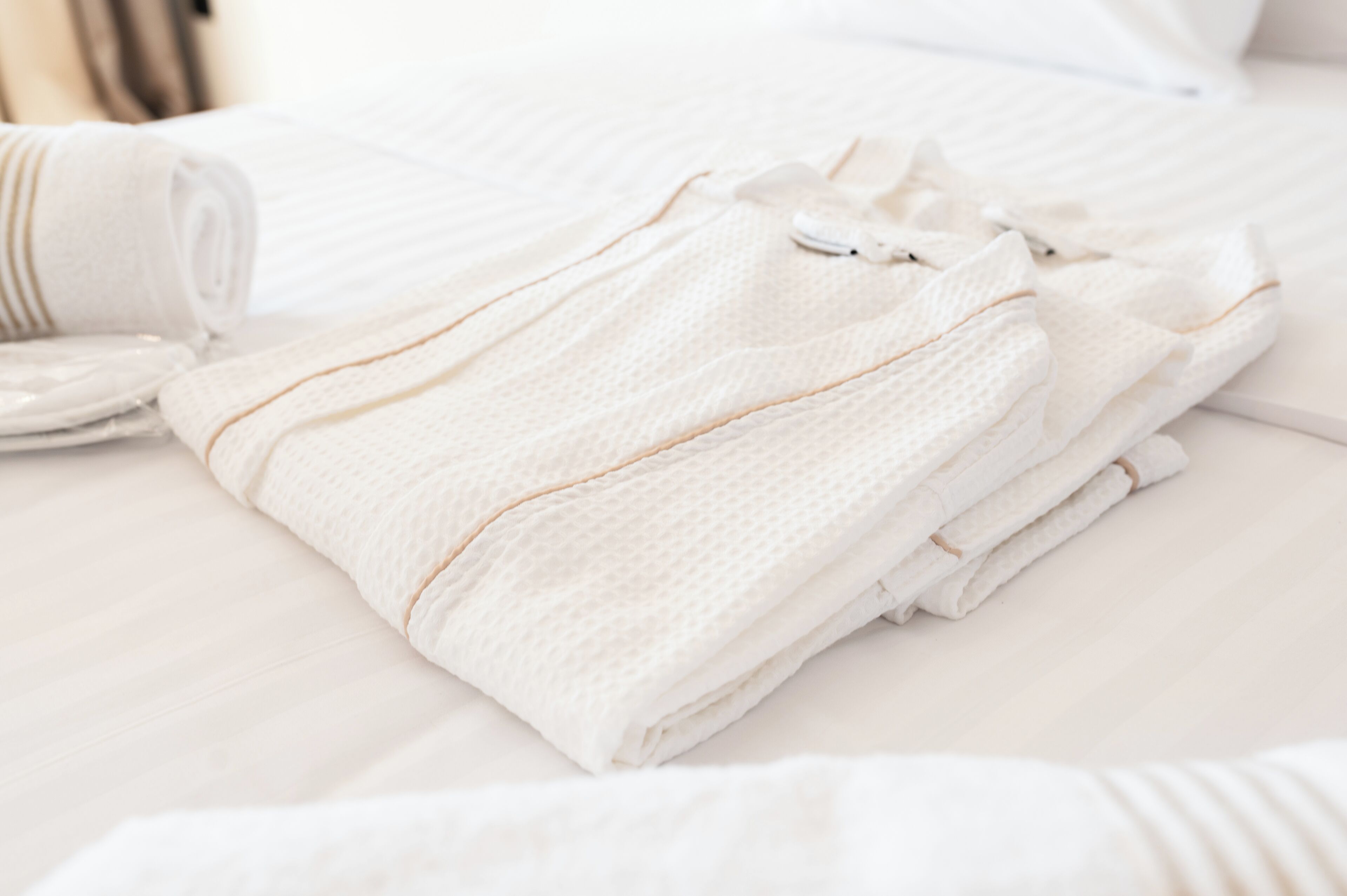 Una toalla blanca doblada con cuidado y un patrón discreto, sobre una cama con colcha a rayas.