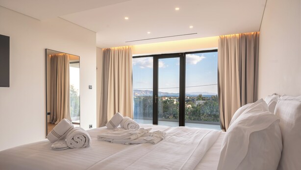 A modern hotel room with a large bed, a balcony with a city view, and a large mirror. - Megara Hotel (Megara)