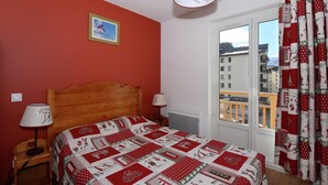Un dormitorio con una cama de madera, una pared roja, una ventana con cortinas y un cuadro en la pared.