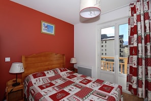 A bedroom with a wooden bed, a red wall, a window with curtains, and a picture on the wall. - Apartment in French Alps for All Group Sizes (Les Deux Alpes)