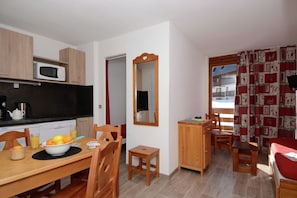 A compact kitchen with a microwave, stove, and a dining area with a table set for two. - Apartment in French Alps for All Group Sizes (Les Deux Alpes)