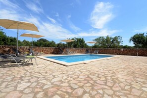 Un espace piscine dallé de pierres, avec des chaises longues et des parasols.