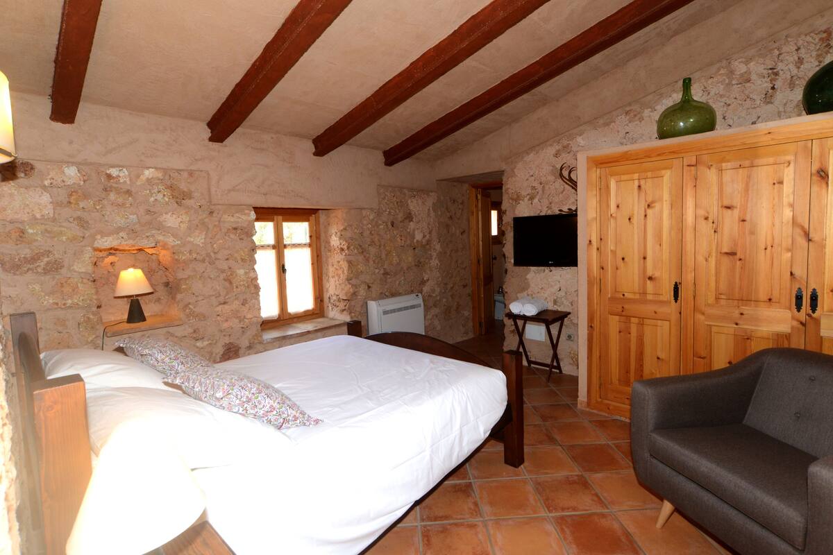 A rustic room with a bed, a wooden cabinet, a television, and a small table.