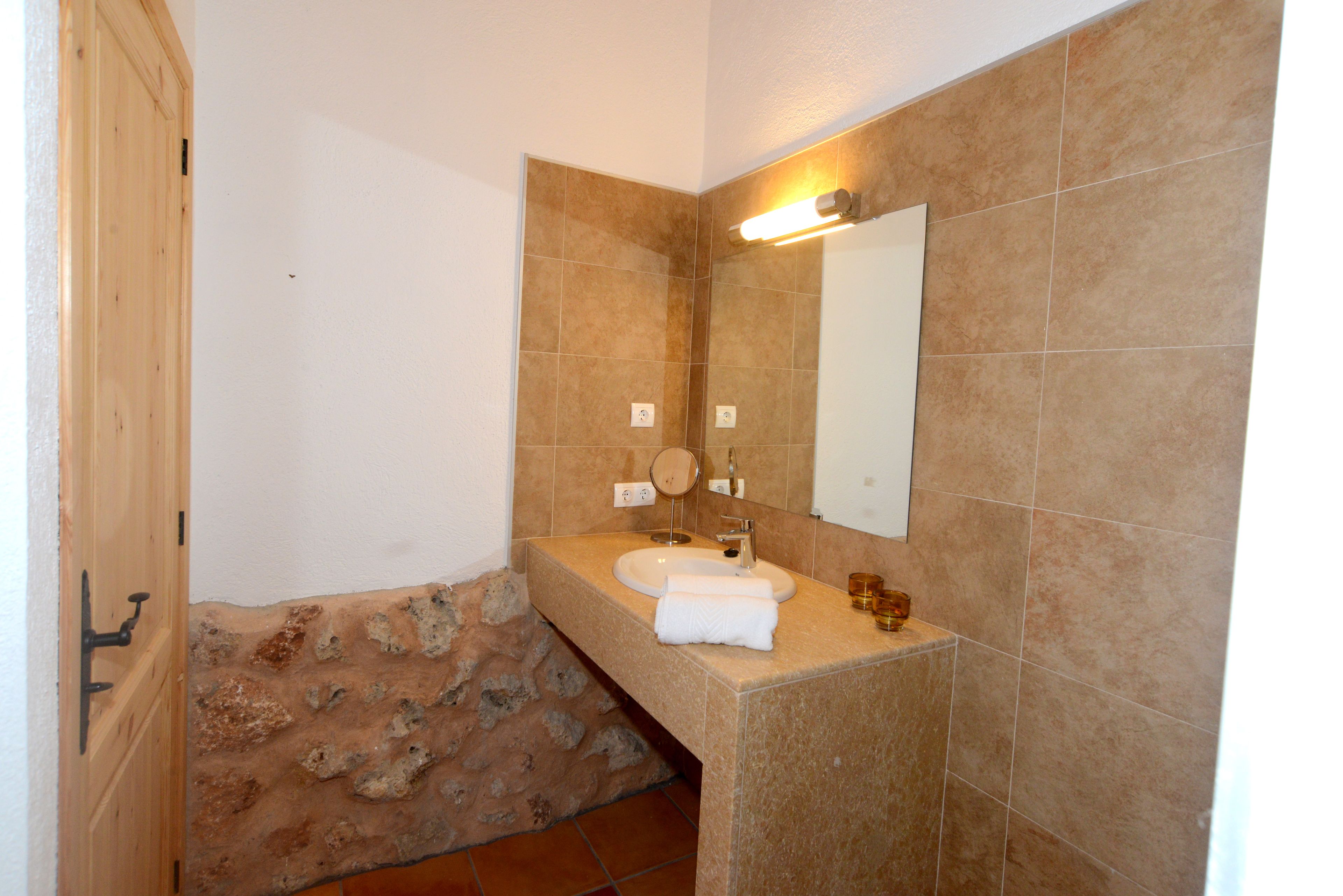 Un baño con pared de piedra, un lavabo, un espejo y una toalla.