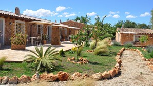 A rustic house with a patio, outdoor seating, and a garden with various plants and a gravel path. - Agroturismo Can Porretí (Lloret de Vistalegre)