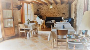 A rustic dining area with wooden tables and chairs, a stone wall, and a wooden ceiling. - Agroturismo Can Porretí (Lloret de Vistalegre)