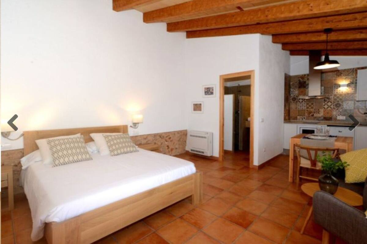 A bedroom with a wooden bed, a small desk, and a kitchenette.