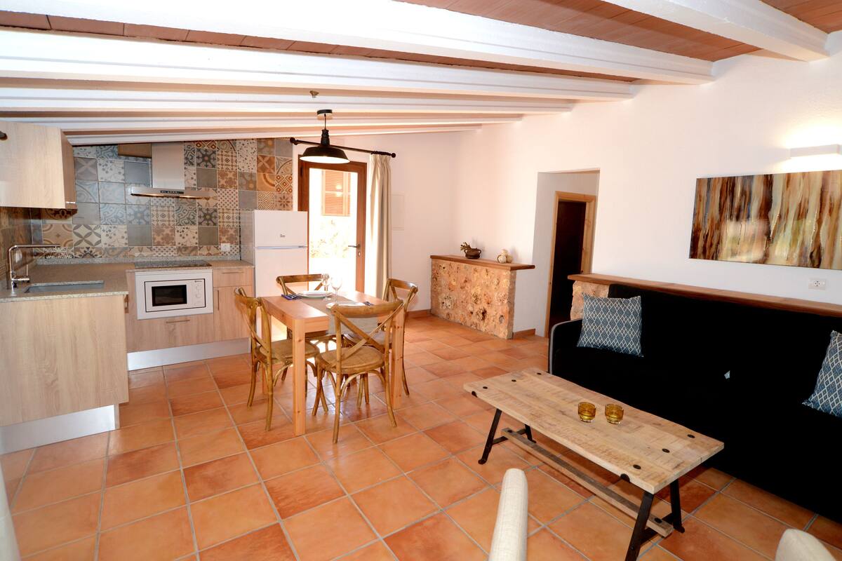 A kitchen with a dining table and chairs, a black sofa, and a tiled floor.