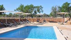 A rectangular swimming pool with lounge chairs and umbrellas, surrounded by stone walls and trees. - Agroturismo Can Porretí (Lloret de Vistalegre)