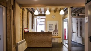 A reception area with a brick counter, hanging pendant lights, a clock, and a welcome sign in multiple languages. - El Albergue de la Catedral - Hostel (Vitoria-Gasteiz)