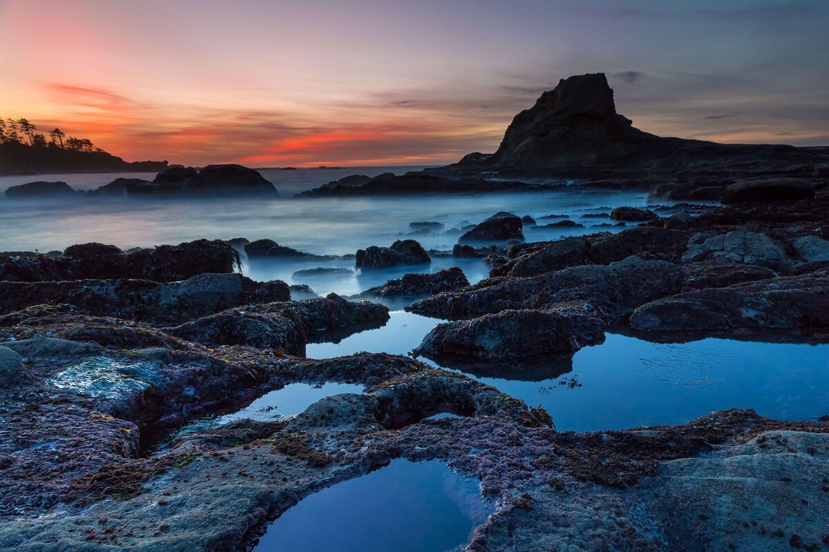 A rocky shoreline with calm water and a sunset.
