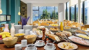 A breakfast buffet with various food items and a view of mountains through large windows.
