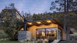 A modern wooden house with a stone base, large windows, and a wooden deck.