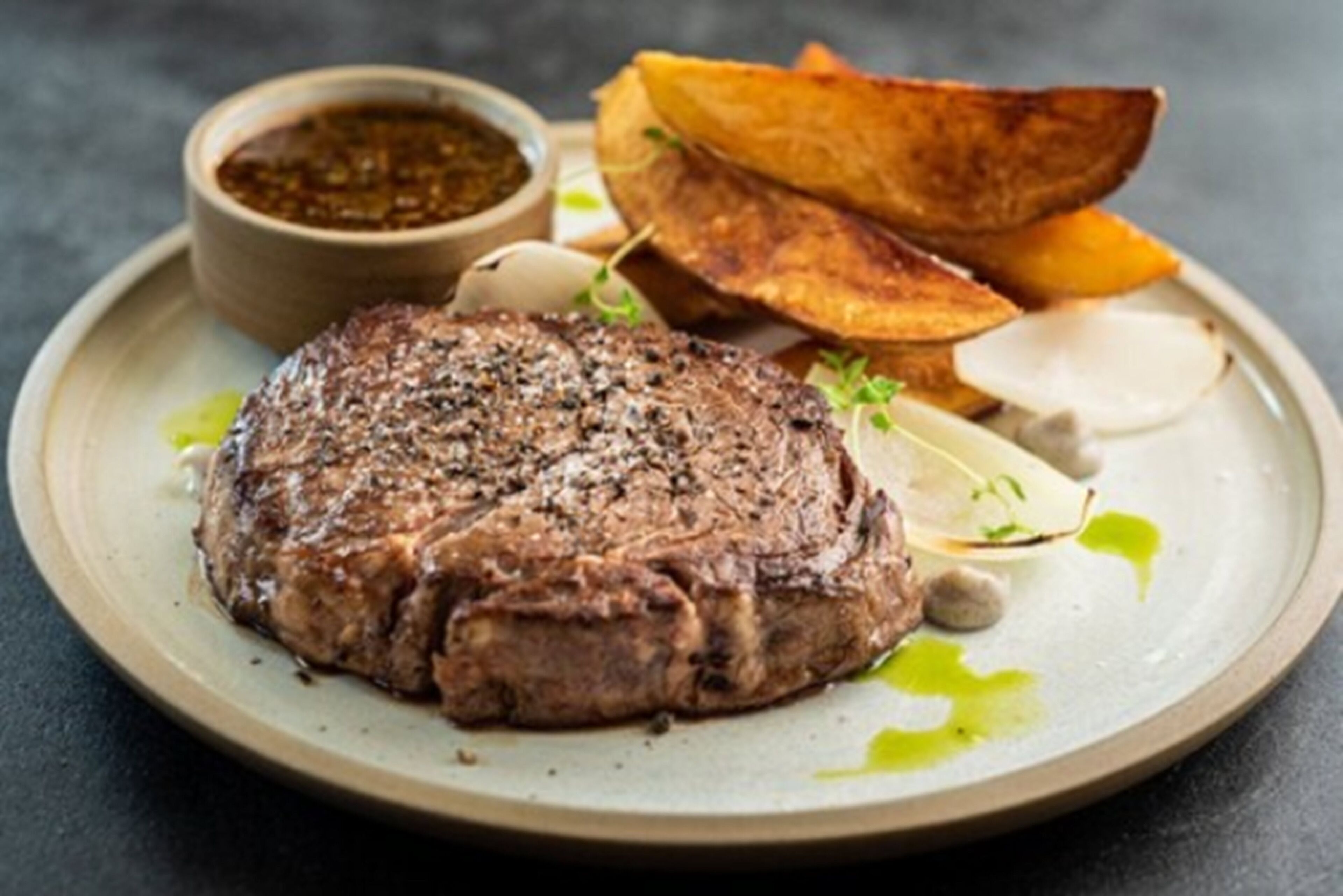A steak with roasted potatoes and a side of vegetables on a plate.