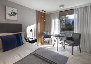 Habitación de hotel moderna con una cama grande, dos sillones, una mesita redonda, vistas a las montañas a través de la ventana y una pared de acento de madera.