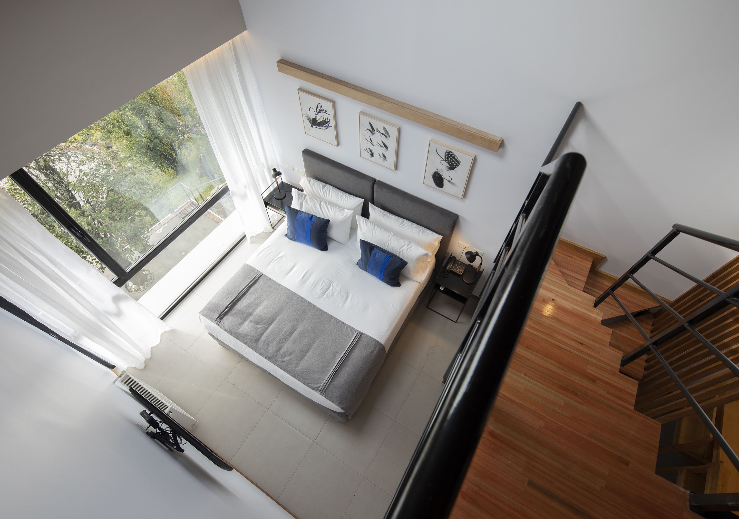 A modern bedroom with a large bed, a nightstand, a window with curtains, and a wooden staircase.