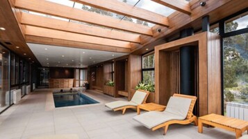 A modern indoor pool area with wooden beams, large windows, and lounge chairs.