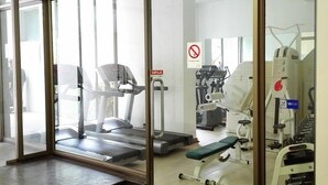 Un gimnasio con equipo de ejercicio, una caminadora y un cartel de prohibición de fumar.