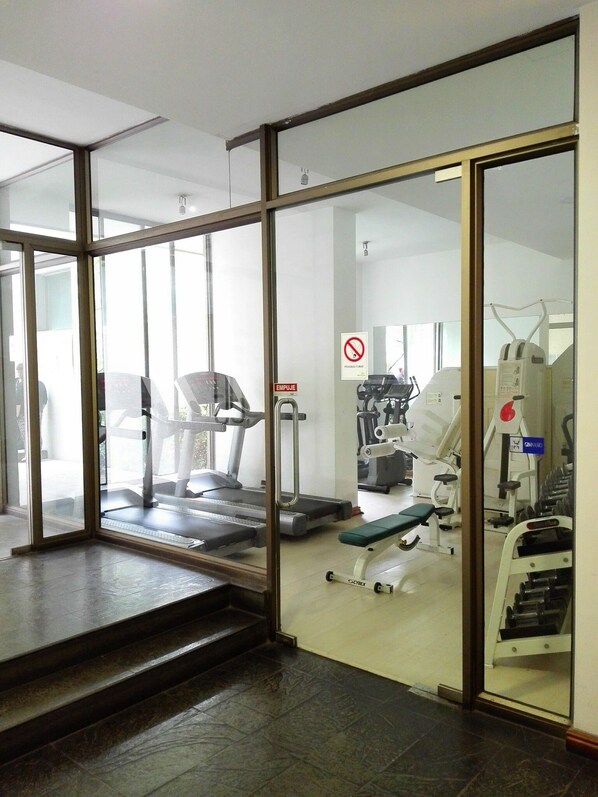 Un gimnasio con equipo de ejercicio, una caminadora y un cartel de prohibición de fumar.