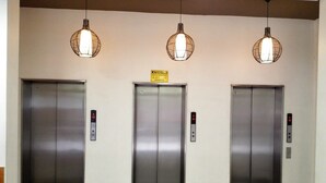 Tres puertas de ascensor con pantallas digitales, un letrero sobre la puerta central y tres lámparas colgantes.