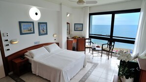 A hotel room with a bed, desk, chair, and a large window with a view of the sea. - Hotel Venus (Gabicce Mare)