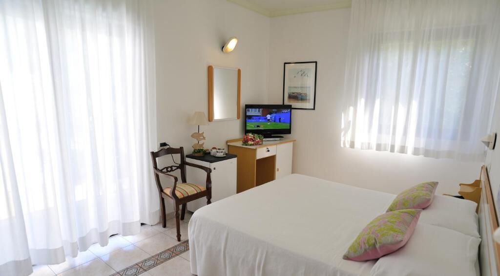 A hotel room with a bed, a desk with a television, a chair, and curtains.