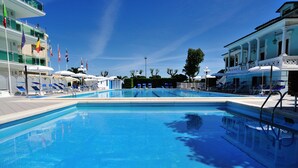 A swimming pool with lounge chairs and umbrellas, surrounded by buildings with balconies and flags. - Hotel Venus (Gabicce Mare)