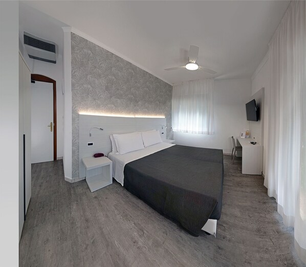 A modern hotel room with a large bed, a bedside table, a nightstand, a ceiling fan, a TV, and a window with curtains. - Hotel Venus (Gabicce Mare)
