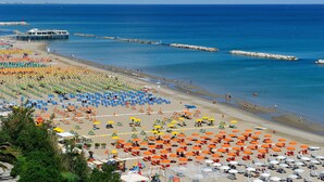 A beach with rows of umbrellas and sun loungers, a pier, and a rocky breakwater. - Hotel Venus (Gabicce Mare)