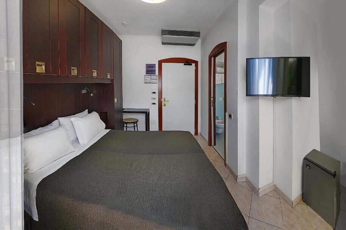 A hotel room with a bed, a desk, a television, and a wardrobe.