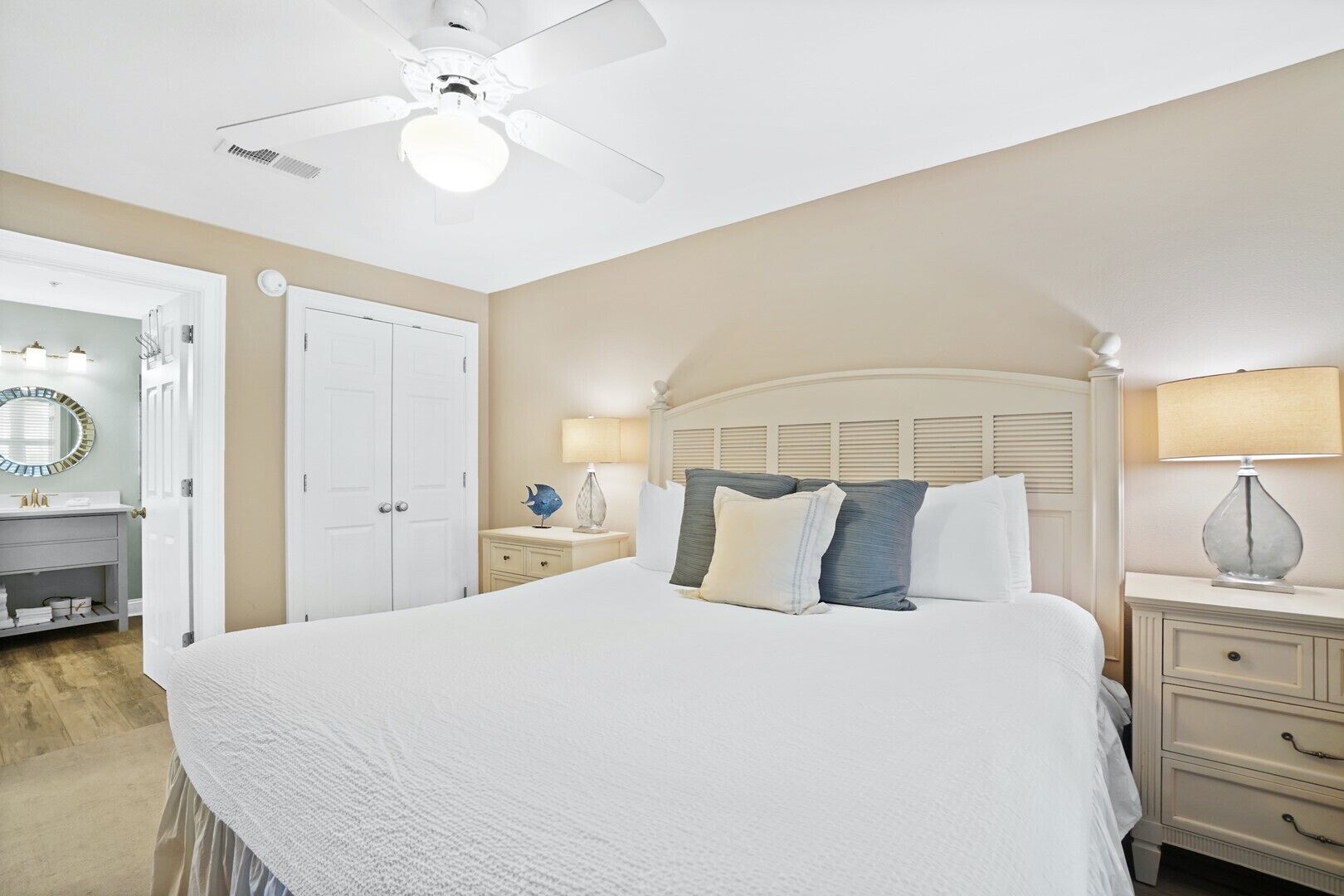 Een slaapkamer met een groot bed, een plafondventilator, een nachtkastje met lamp en een dressoir.
