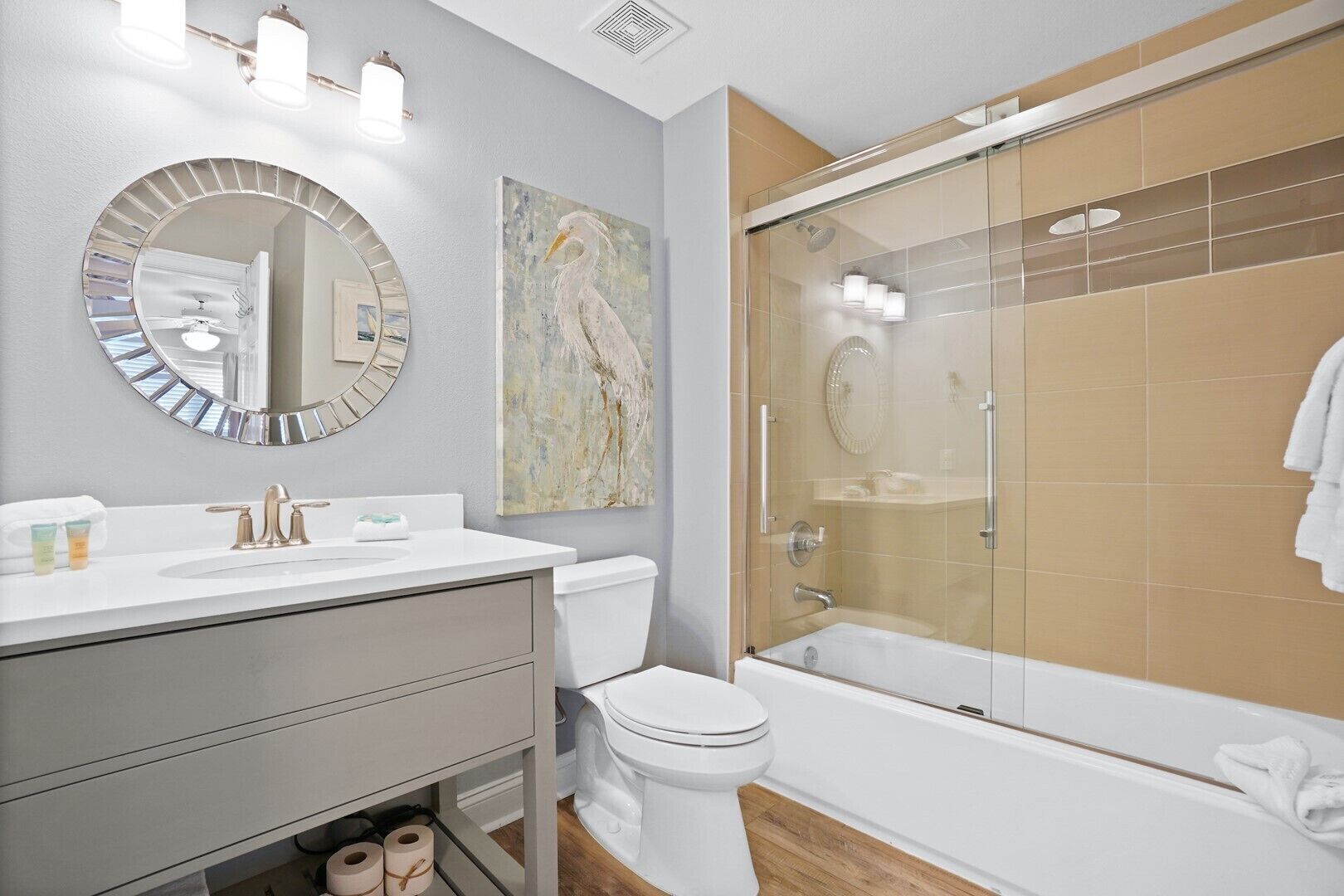 A modern bathroom with a round mirror, a toilet, a bathtub, and a glass-enclosed shower.