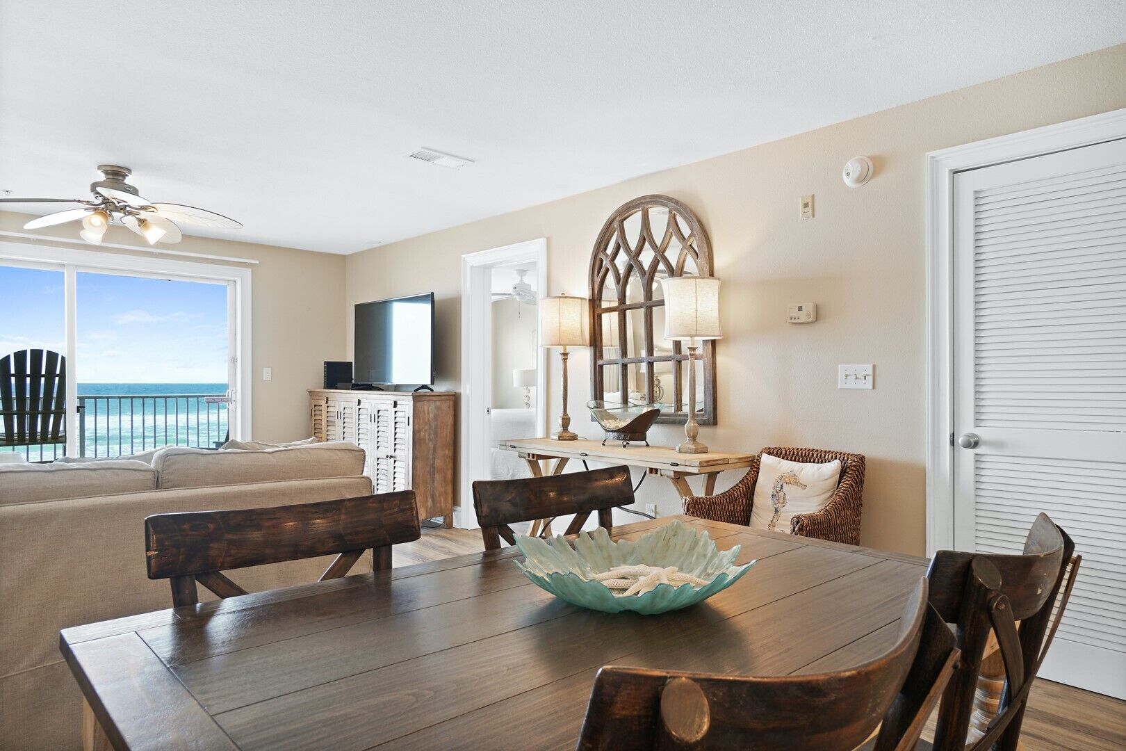 A living room with a view of the ocean, a dining area with a table and chairs, and a TV on a cabinet.