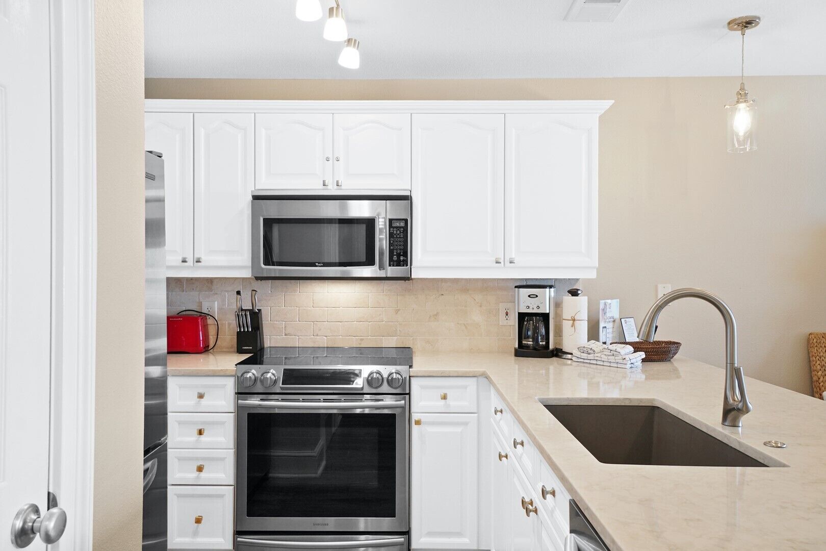 A modern kitchen with white cabinets, stainless steel appliances, a double sink, and a coffee maker.