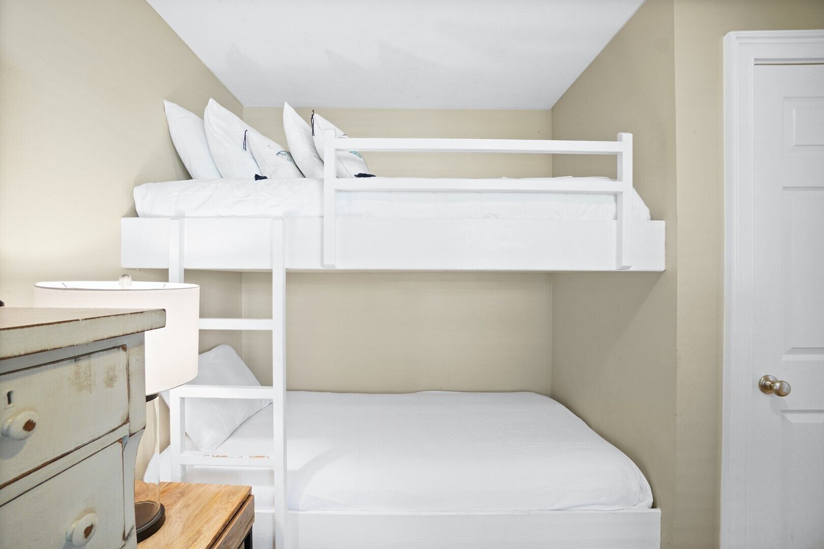Una cama individual con ropa de cama blanca y almohadas, un aparador con cajones y una puerta.
