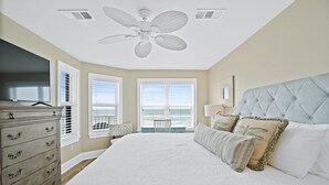 Une chambre à coucher avec un grand lit, un ventilateur de plafond, une commode et un téléviseur.