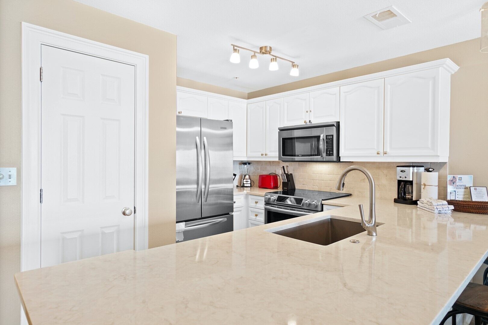 A modern kitchen with white cabinetry, stainless steel appliances, a central island with a sink, and a coffee maker.