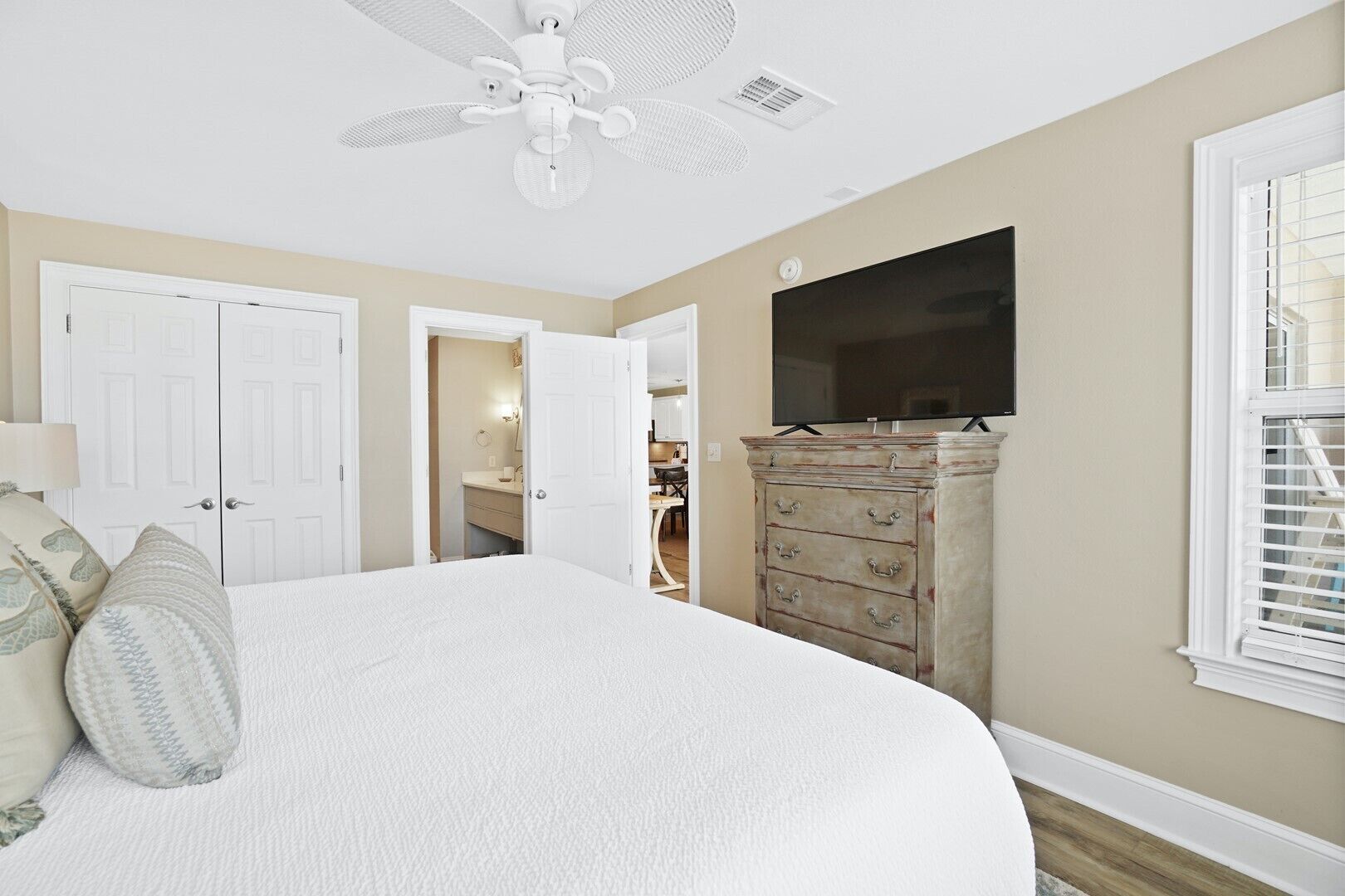 A bedroom with a large bed, a ceiling fan, a dresser, and a TV mounted on the wall.