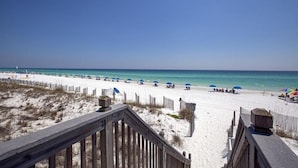 Une plage avec une promenade en bois menant au rivage, une plage de sable et des parasols.