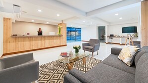 A modern hotel lobby with a reception desk, seating area, and a large window offering a view of the outside. - Hotel Blue 66 (Cali)