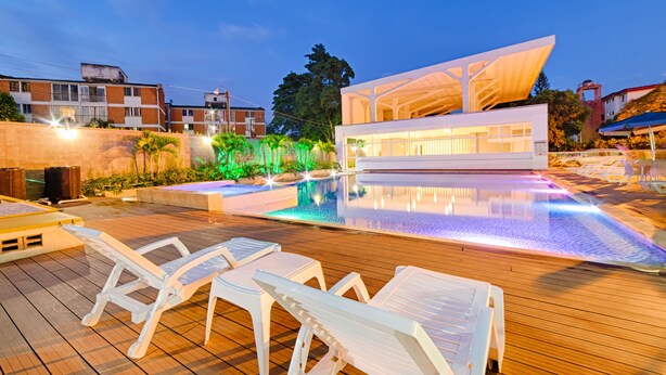 A modern pool area with lounge chairs, a clear pool, and a contemporary building with large windows. - Hotel Blue 66 (Cali)