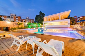 Un área de piscina moderna con sillones de descanso, piscina cristalina y un edificio contemporáneo con grandes ventanales.