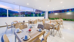 A dining area with tables set for four, large windows, and a view of buildings and greenery. - Hotel Blue 66 (Cali)