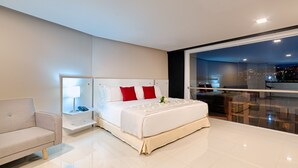 A modern hotel room with a large bed, a nightstand, a bedside table, a chair, and a large window with a city view. - Hotel Blue 66 (Cali)