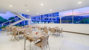 A modern dining area with tables and chairs, a staircase, and large windows offering a view of the outdoors. - Hotel Blue 66 (Cali)