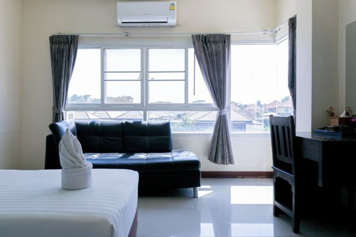 A hotel room with a bed, a sofa, a desk, and a window with curtains.