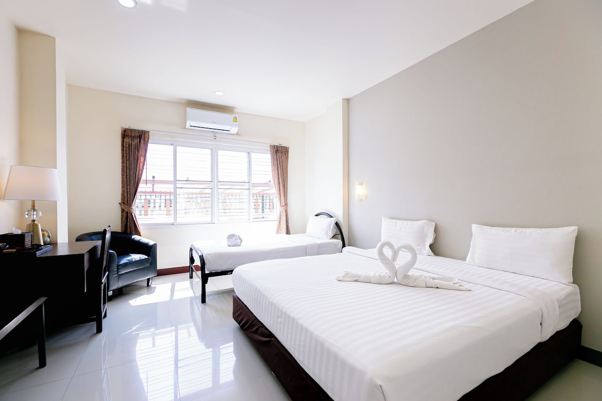 A hotel room with two beds, a desk, a chair, a lamp, and a window with curtains.