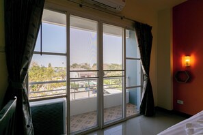 Una habitación con un amplio ventanal corredero que da a un balcón, una cama, una lámpara fijada a la pared y un equipo de aire acondicionado.
