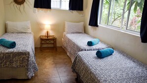 A room with two single beds, each with a patterned bedspread and a rolled towel. There is a small wooden nightstand with a lamp between the beds. - Whitehouse Apartments Rarotonga (Rarotonga)